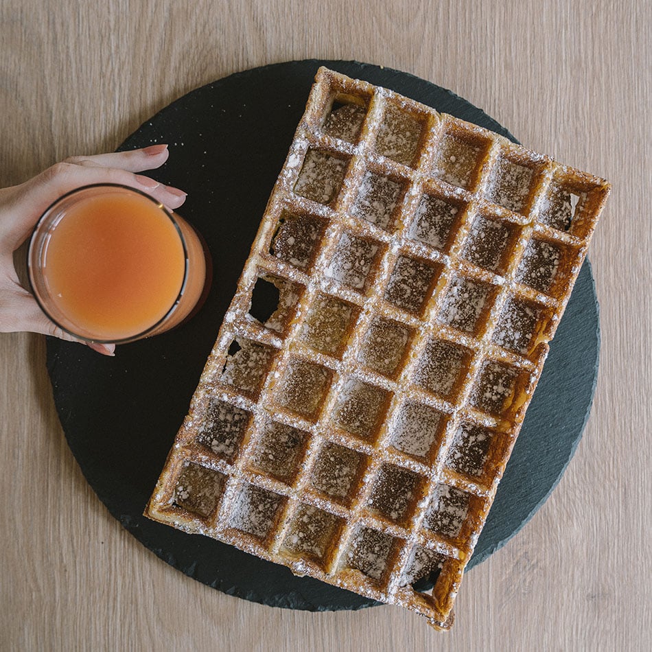 Gaufre géante sur une ardoise ronde avec un verre de jus d'orange